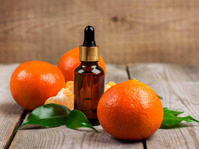 A small dropper bottle of tangerine oil with whole and halved oranges and leaves on a wooden table