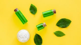 茶树油和叶子的容器和一碗海盐的黄色背景