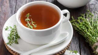一杯白色的百里香茶,上面放着方糖和百里香,背景是木质的
