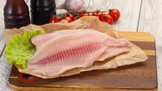 罗非鱼在羊皮纸鱼片,生菜,西红柿,大蒜在后台