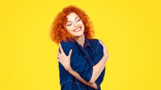 一个女人在黄色的背景下拥抱着自己,脸上带着微笑