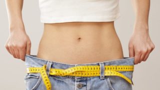 一个女人拿着一大牛仔裤搂着她的腰,以显示多少重量,她已经失去了