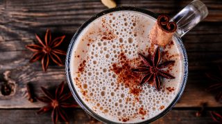 自制的印度茶拿铁与茴芹和肉桂棒在玻璃杯在木制乡村背景