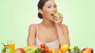 女子咬一个苹果,坐在水果的分类的前面。