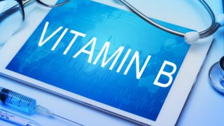 “维生素B”字样写在一张标签上,旁边是听诊器、注射器和眼镜,放在蓝色的表面上。