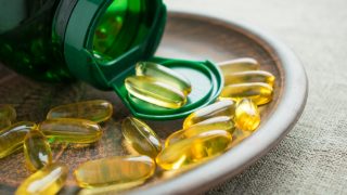 补充维生素D3的黄色胶囊放在一个打开的瓶子旁边的盘子里