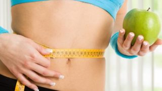 女子测量她用卷尺腰,拿着一个苹果。