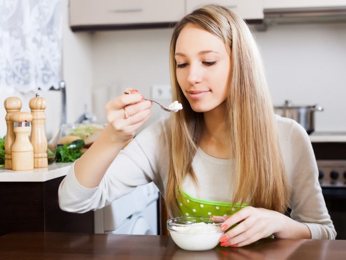 一个年轻的女人在厨房里用勺子吃软干酪