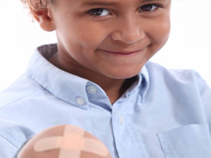 Close up of a young smiling boy who is showing his wound on the knee