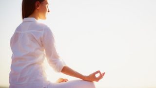 一名身穿白色衣服的年轻女子坐在沙滩上做莲花式瑜伽练习