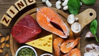 富含锌的食物(切的三文鱼,肉,虾,大蒜,蘑菇,杏仁,腰果,菠菜,&豆类)在一张木桌上