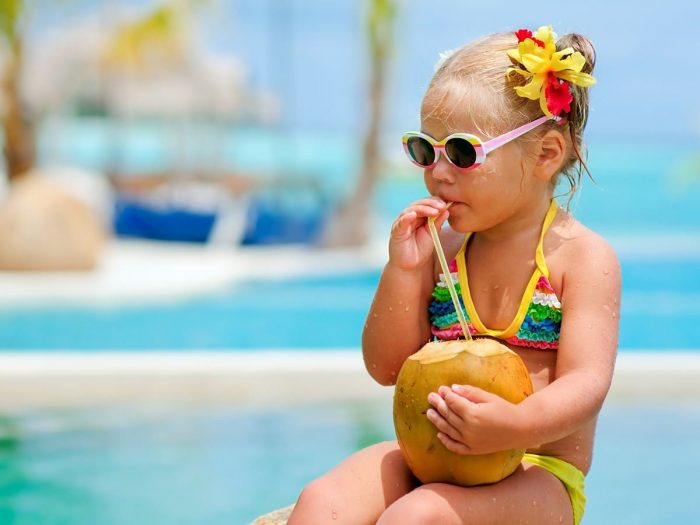 一个小女孩穿着五颜六色的泳衣在游泳池附近喝椰子汁