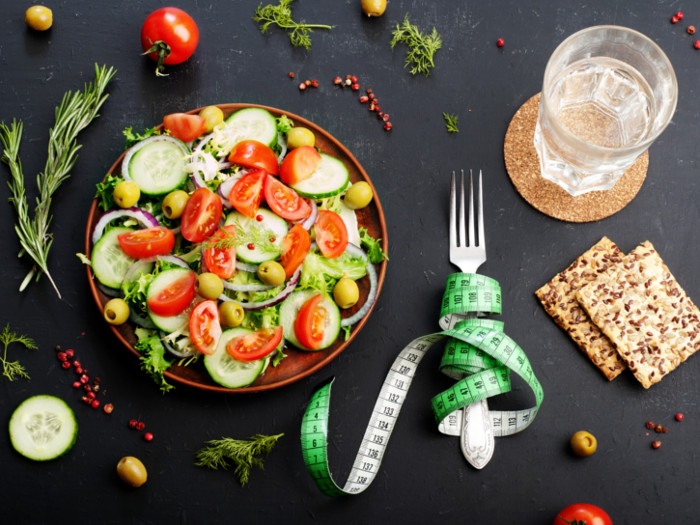 沙拉，饼干，一杯水和叉子在卷尺卷曲，在板岩背景。