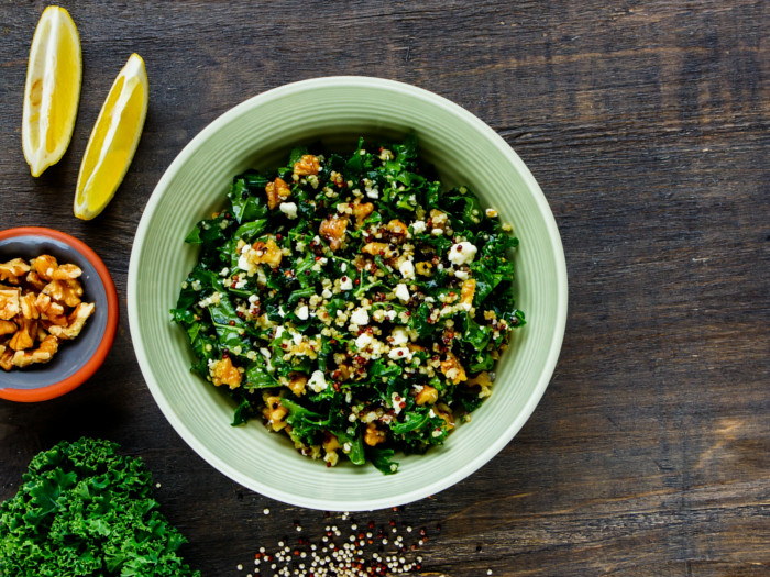 羽衣甘蓝和quinoa salad in a bowl on a brown table top with lemon, broccoli, and walnuts