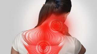 一名年轻女子面对墙壁，双手托着脖子，肌肉疼痛