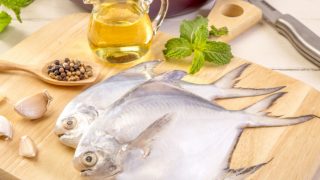 Pompano鱼在木砧板上，背景是一个油瓶和香料