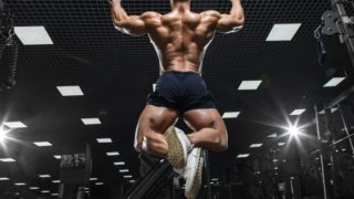 一个男人穿着短裤在健身房做引体向上的后视图。