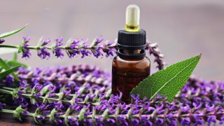 木桌上放着一小滴鼠尾草油和新鲜的鼠尾草花和叶子