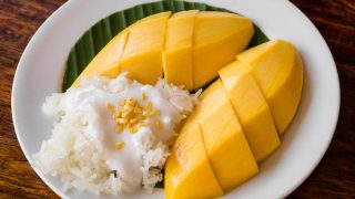 芒果，椰子肉和黏米饭在一个白色盘的香蕉叶子