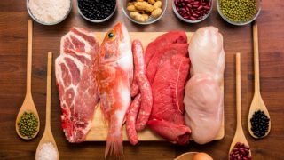 不同种类的新鲜生肉(鱼、猪肉、牛肉、鸡肉和红肉)和未煮过的蛋白质(豆类、坚果、米饭和鸡蛋)放在一张木桌上