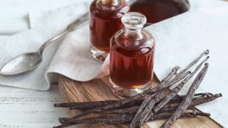 在新鲜的香草豆和一碗香草提取物旁边的两个香草萃取瓶与匙子