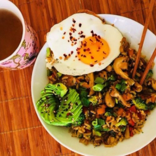 炒蔬菜用米饭炒米饭，配上鳄梨和鸡蛋到侧面，放置在一张木桌子上