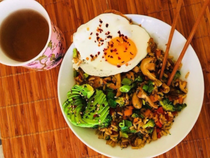 炒蔬菜用米饭炒米饭，配上鳄梨和鸡蛋到侧面，放置在一张木桌子上
