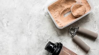 乳清蛋白粉，一个瓶子和手压在白色的灰色背景